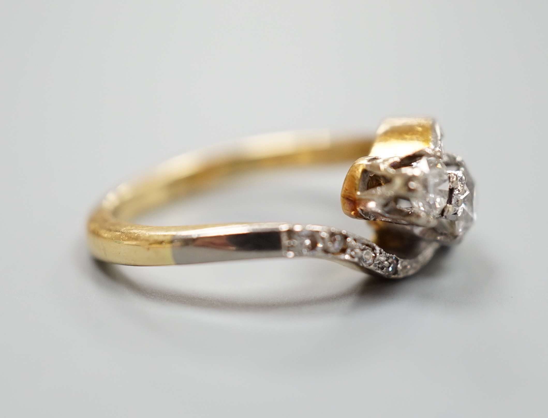 A yellow metal and three stone diamond set crossover ring, with diamond set shoulders, size I, gross 4.6 grams.